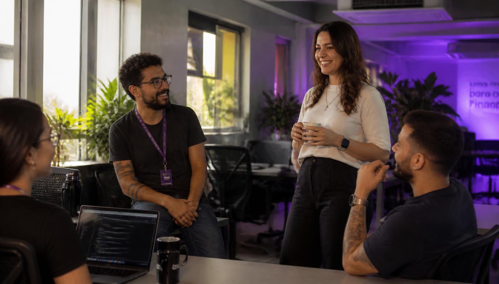 Equipe conversando de forma acolhedora em escritório iluminado por luz natural em tons violeta